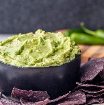 Angle shot of creamy guacamole in a black bowl with chips.