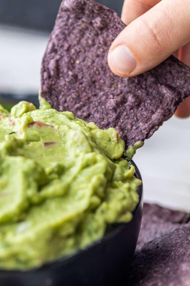 Hand dipping blue chip into avocado dip.
