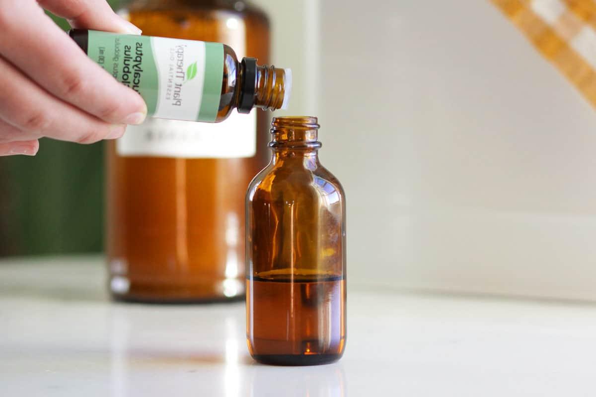 eucalyptus essential oil being added to a small glass amber dropper bottle