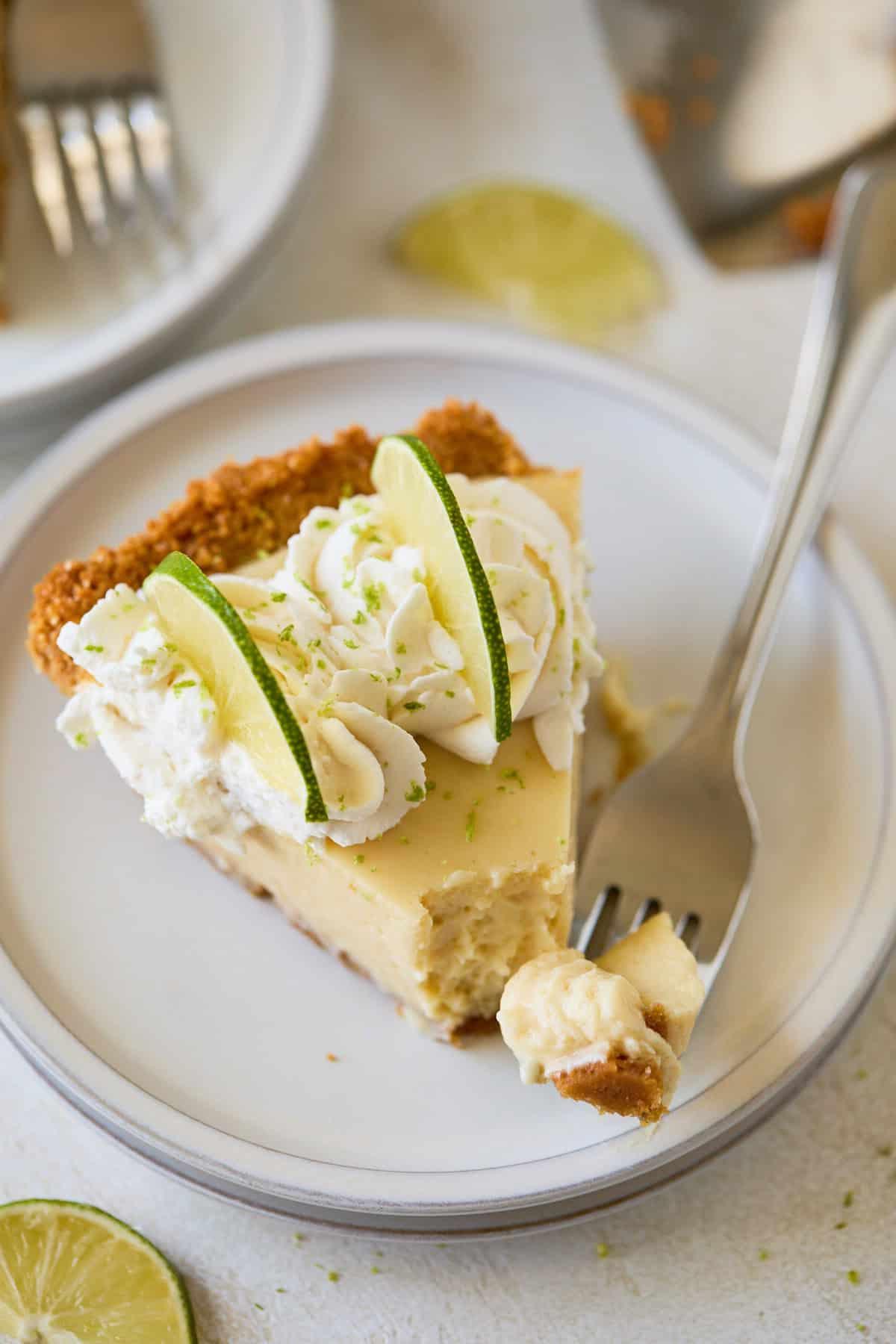 A slice of Key Lime Pie on a white plate, with a bite taken out and a fork beside it.