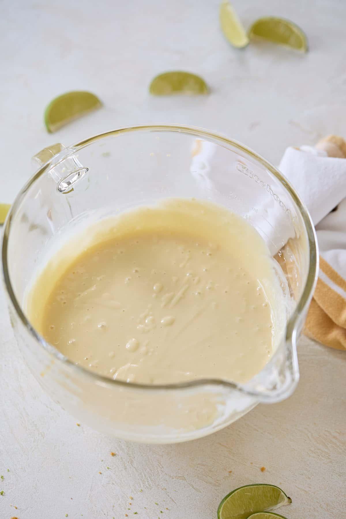 Pie filling mixture in a clear glass mixing bowl with lime slices in the background.