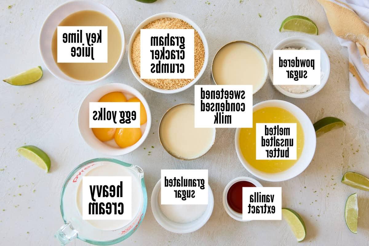 Ingredients for Key Lime Pie arranged on a white surface, including graham cracker crumbs, egg yolks, and sweetened condensed milk.