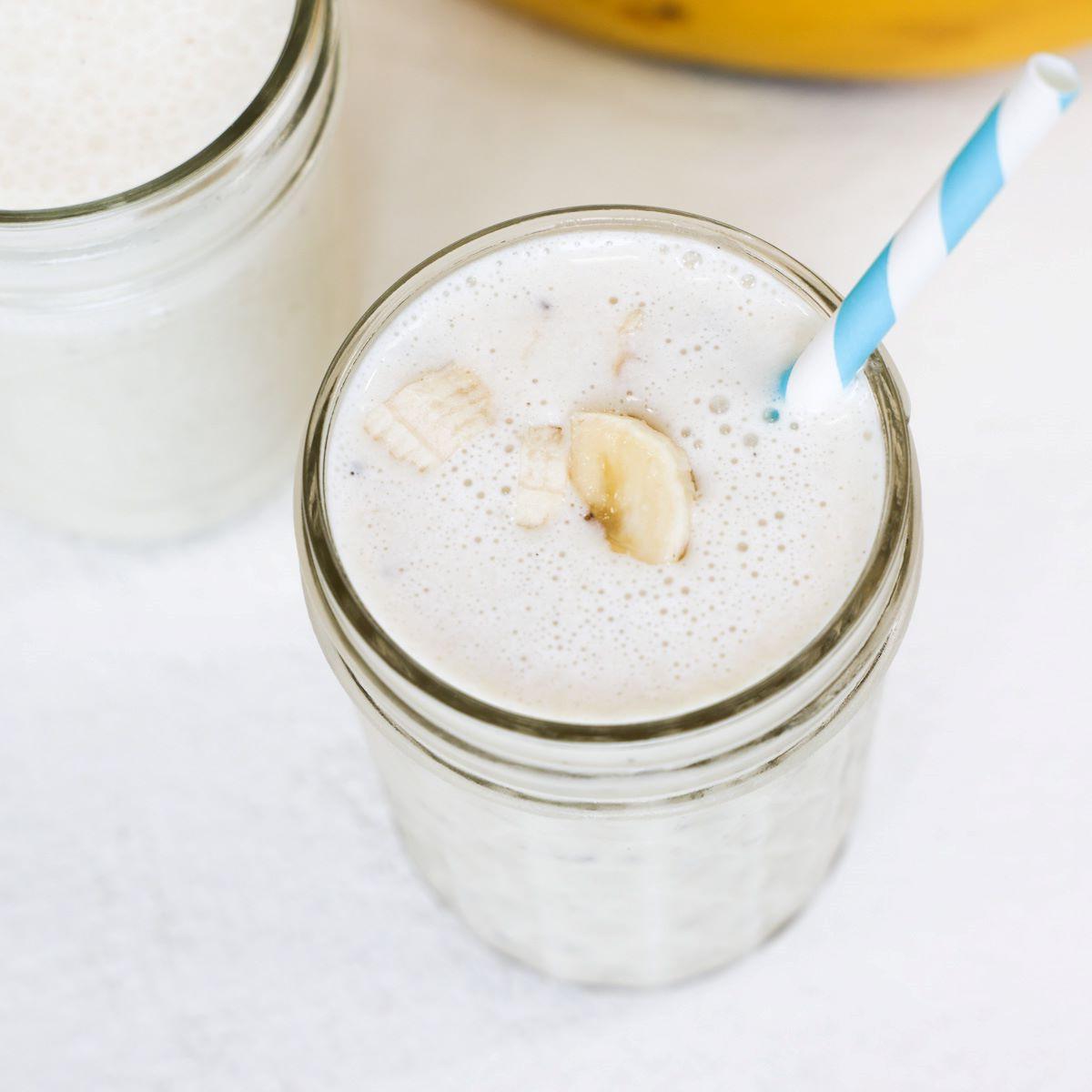 Banana milkshake in a glass topped with banana pieces and served with a blue and white striped straw.